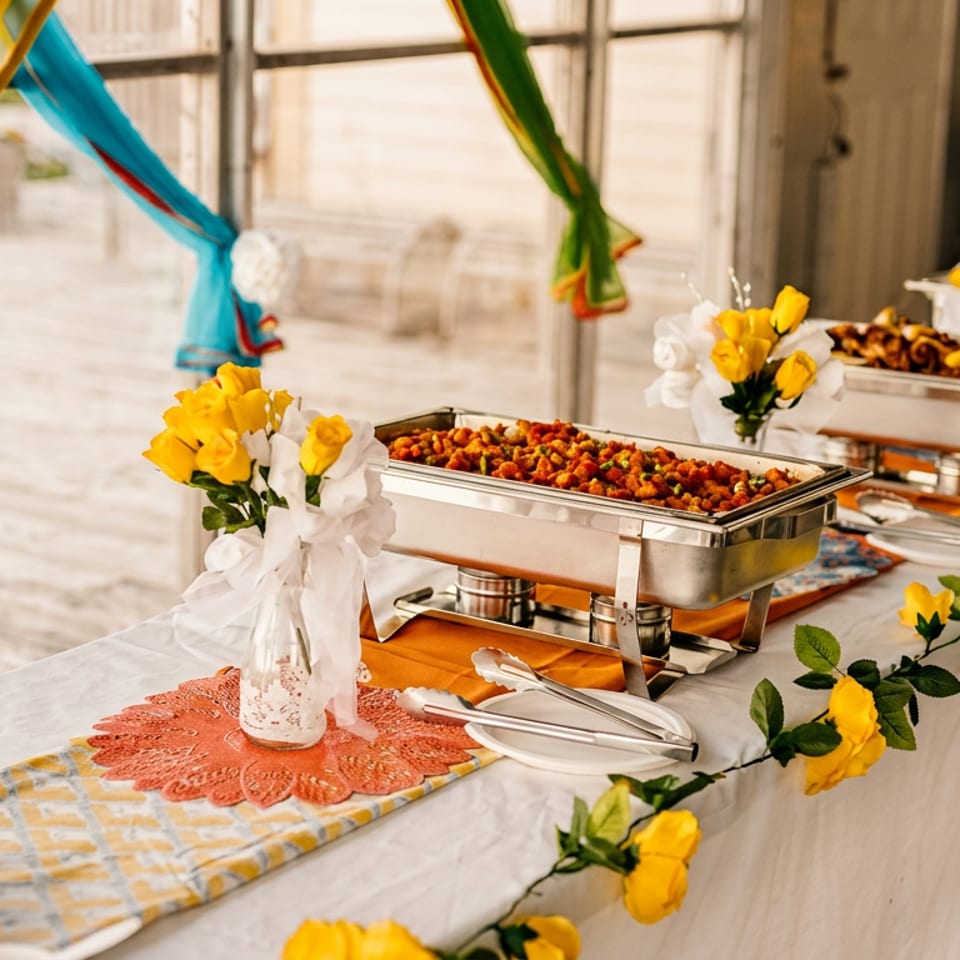 Vibrant Indian buffet table with chafing dishes, sauces, and yellow floral decorations.
