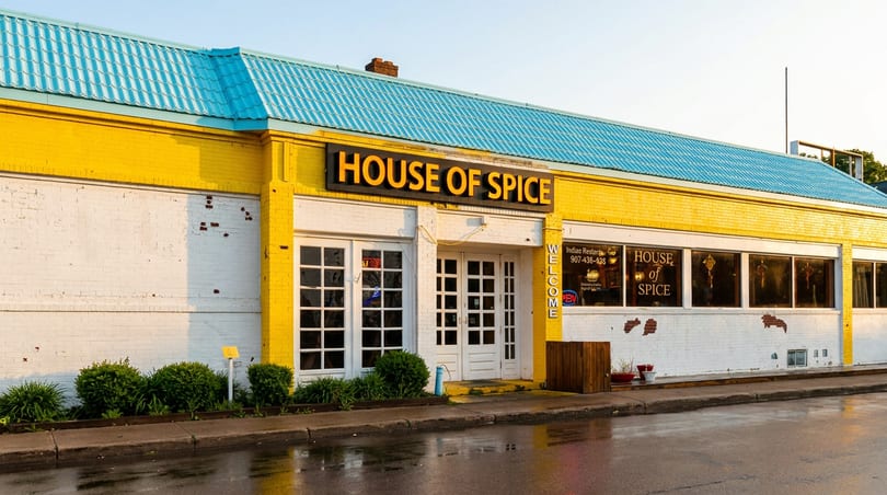 House of Spice restaurant exterior with bright yellow walls, blue roof, white doors, and wet pavement.