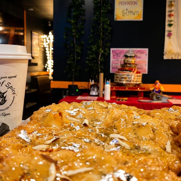 Glazed Indian sweets with almonds and silver leaf, beside a 'House of Spice' cup in a restaurant.