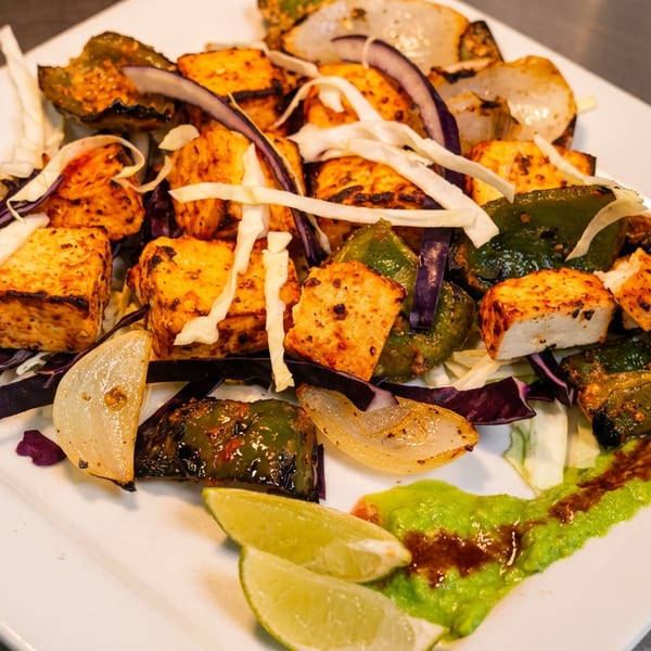 Grilled paneer, bell peppers, and onions with green sauce and lime wedges on a white plate.
