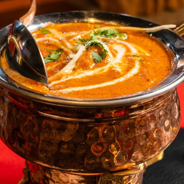 Rich orange curry with cream swirls and green garnish in a traditional copper serving pot.