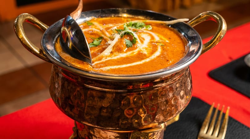 Rich orange curry with cream swirls and green garnish in a traditional copper serving pot.