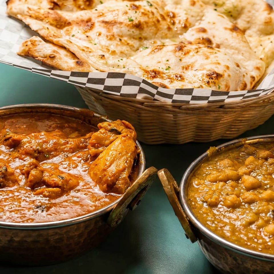 Chicken curry, chickpea curry, and naan bread served in traditional bowls and a basket.