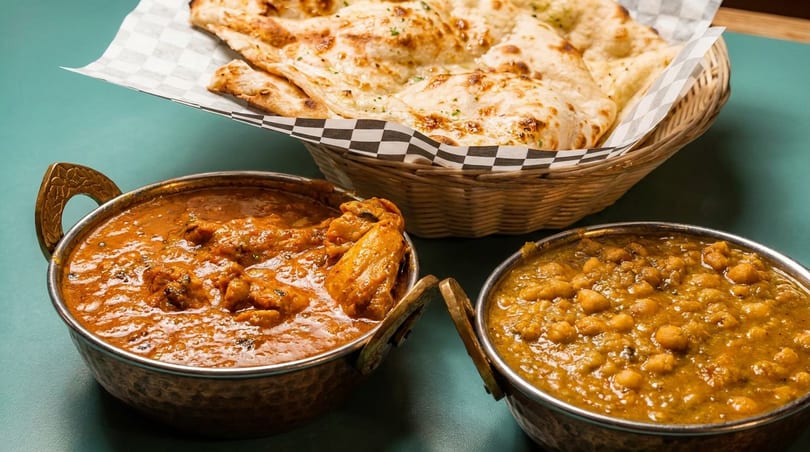 Chicken curry, chickpea curry, and naan bread served in traditional bowls and a basket.