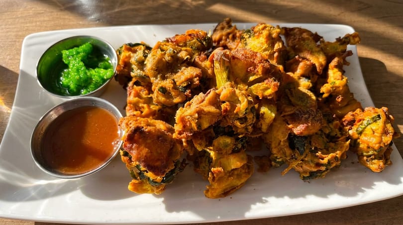 Plate of golden-brown pakoras with green chutney and tamarind sauce on a white plate.