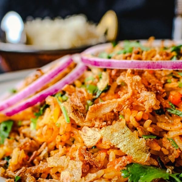 Vibrant biryani rice topped with red onion, crispy fried onions, and fresh green herbs on a white plate.