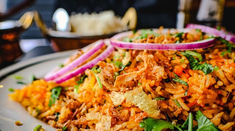 Vibrant biryani rice topped with red onion, crispy fried onions, and fresh green herbs on a white plate.